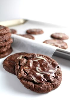 chocolate cookies with white frosting on a plate next to a cookie sheet and knife