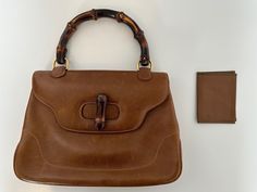 This 70s Gucci Bamboo 1947 small top handle bag, is a vintage treasure crafted in Italy from rich tan brown leather with gold-plated hardware. The iconic bamboo handle gives it a distinctive character.  While pre-owned with visible signs of use, it remains undamaged and in very good condition, offering a sense of history without compromising its functionality or beauty.  The interior is lined with smooth leather, complete with inner pockets for organization.  Included is the original Gucci card 70s Gucci, Gucci Bamboo 1947, Small Top Handle Bag, Treasure Crafts, Gucci Bamboo, Bamboo Handles, 70s Vintage, Handle Bag, Leather Top