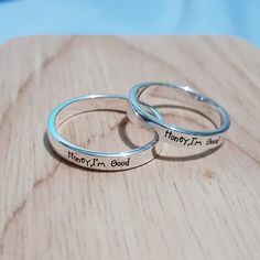 two silver rings with handwriting on them sitting on top of a wooden table next to each other