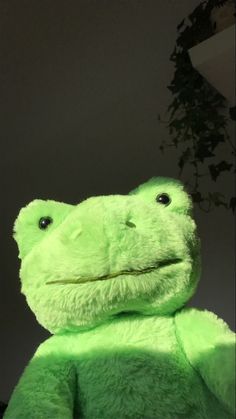 a green frog stuffed animal sitting next to a potted plant