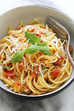 a bowl filled with pasta and topped with parmesan cheese, tomatoes and basil