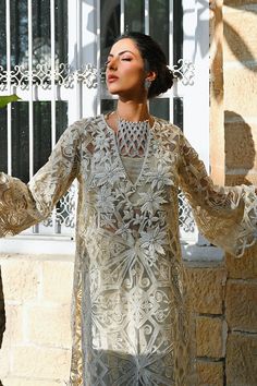 Radiate splendour in this ivory handworked long tulle shirt enhanced through the use of sequins and cutwork details on the sleeves. Paired with a pale bone hued charmeuse choli featuring cutwork details and a matching skirt. Model Height is 5'10 and shirt length is 46"