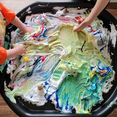 two children are playing with paint in a black tray