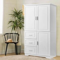 a white armoire next to a chair and potted plant