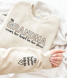 "Custom Sweatshirt for Grandma, Christmas Gift for Grandma, I Wear My Heart On My Sleeve, Grandma Sweatshirt with Grandkids Name on Sleeve This custom sweatshirt for grandma is the perfect Christmas gift to show her how much you care. Featuring the heartwarming phrase \"I Wear My Heart On My Sleeve,\" this sweatshirt is sure to make grandma feel loved and appreciated. Personalized with grandkids names on sleeve High-quality material for maximum comfort Unique and thoughtful gift idea Made with high-quality material, this grandma sweatshirt is soft, cozy, and perfect for keeping warm on chilly days. The personalized touch of adding grandkids' names on the sleeve makes it a truly special gift that she's sure to cherish forever. This custom sweatshirt comes in various sizes and colors, ensuri What To Get Your Grandma For Christmas, Personalized White Tops For Winter, Personalized Tops As Fall Gifts, Winter Name Print Top As Gift, Custom Text Long Sleeve Tops For Gifts, Name Print Tops As Winter Gift, Personalized Crew Neck Top For Gift, Personalized Crew Neck Tops For Gifts, Personalized Long Sleeve White Tops