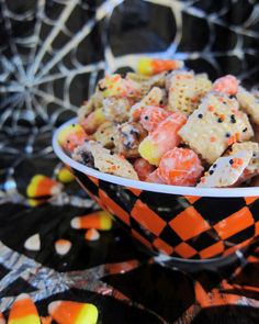 a bowl filled with halloween chex mix on top of a black and orange table cloth