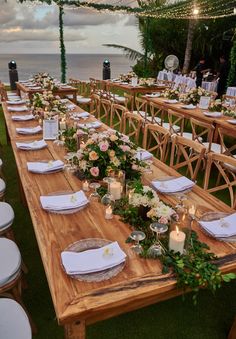 a long wooden table with white plates and flowers on it is set for an outdoor dinner