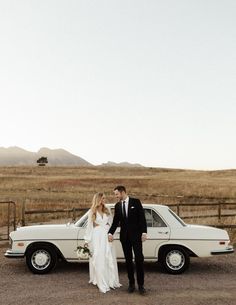 a bride and groom standing in front of a white car