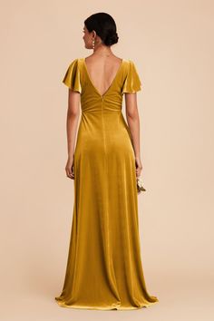 the back of a woman wearing a gold dress with ruffle sleeves and open shoulders