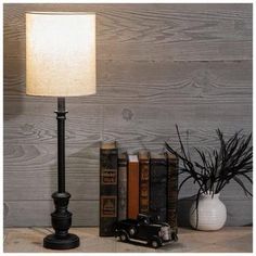 a lamp on a table next to some books and a vase with plants in it