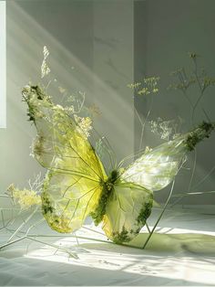 a yellow butterfly sitting on top of a white floor next to plants and flowers in the sunlight