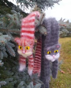 two cat ornaments hanging from a tree in the grass, one is wearing a striped scarf