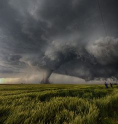 a group of people standing on top of a lush green field under a storm cloud