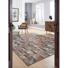 an open door leading to a living room with white walls and wooden floors, along with a multicolored rug on the floor