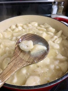 a wooden spoon in a pot filled with macaroni and cheese on the stove