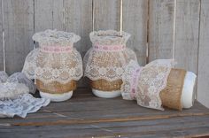 three vases with lace on them are sitting on a wooden table next to some burlocks