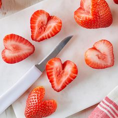 strawberries cut into heart shapes on a cutting board next to a knife and napkin