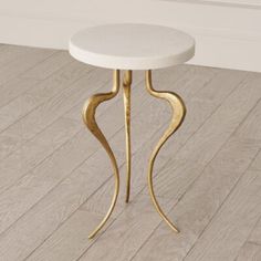 a small white table with gold legs and a marble top on a wooden floor in a room