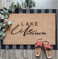 a pair of sandals sitting on top of a door mat that says lake life is the best life