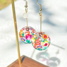 Hand Painted Plant and Flower on Glass Globe Drop Earrings The plant and flowers are hand-painted on the glass globe. In the center of the glass globe, there is a garnet bead, which makes the globe dangle freely. The earrings are finished with white moonstones.  As a gift shop, we offer a complimentary gift box for every order. Detail:  size of one earring - around 20mm*60mm;  size of moonstone: around 6mm size of garnet: around 4mm  Material:  globe - glass;  beads - moonstone, garnet;  ear wires - gold-plated sterling silver. About postage Standard postage  When choosing standard postage, we assume this order is for yourself, or you will wrap the item yourself before giving it out as a gift (the complimentary gift box would be posted flat with your order under standard postage). Hence, t Multicolor Round Flower Earrings, Round Resin Flower Earrings, Glass Drop Earrings, White Moonstone, June Birth Stone, Glass Globe, Moon Stone, Gold Plated Sterling Silver, Flower Painting