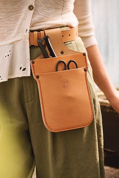 a woman is holding a leather case with scissors in it