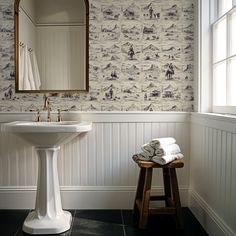 a white sink sitting under a bathroom mirror next to a wooden stool with towels on it