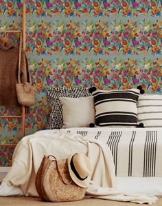 a bedroom with colorful wallpaper and pillows on the bed, along with a straw bag