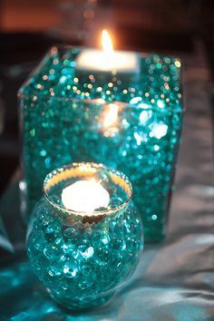 two candles sitting on top of a table next to each other in glass vases