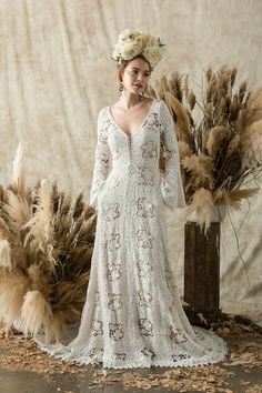 a woman wearing a white dress standing in front of some dried grass and flowers on her head