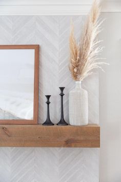 a white vase sitting on top of a wooden shelf next to two black candles and a mirror