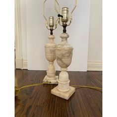 two white marble vases sitting on top of a wooden floor