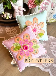 two decorative pillows sitting on top of a wooden table next to potted plants and flowers