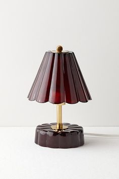 a red lamp with a gold base on a white tableclothed surface, in front of a plain wall