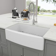 a white kitchen sink sitting under a window next to a toaster and coffee maker