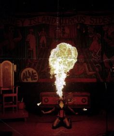 a woman sitting on the ground with fire in her hand and an advertisement behind her