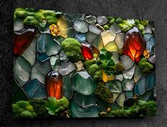 a piece of art made out of stained glass and green plants on the side of a wall