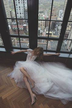 a woman in a white dress is sitting on the floor by a window with her arms outstretched