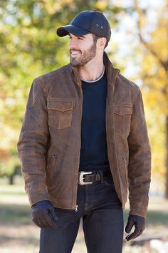 a man with a hat and gloves standing in the park wearing a brown leather jacket