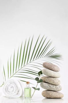 a white table topped with stones and a palm leaf next to a bottle of lotion