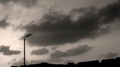 black and white photo of the sky with clouds above buildings in front of a street light