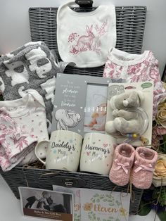 a basket filled with baby's clothes and books next to a teddy bear, bib and booties