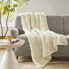 a living room with a gray couch and white knitted blanket on top of it