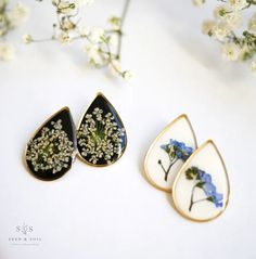 three pieces of jewelry sitting next to each other on a white surface with flowers in the background