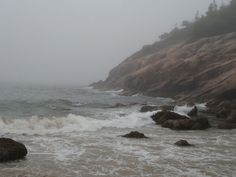 the waves are crashing on the rocky shore in the foggy day at the beach