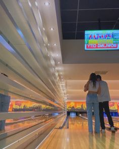 two people are standing in an empty bowling alley with their backs to each other and looking at the television screen above them