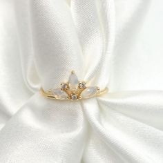 a gold ring with white stones sits on top of a white satin material, surrounded by small diamonds