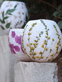 three white vases with flowers painted on them sitting next to each other in front of some bushes