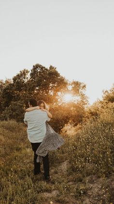 a man carrying a woman in his arms while standing on a hill with the sun behind him