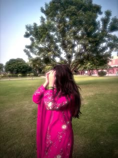 a woman in a pink dress looking up at a tree