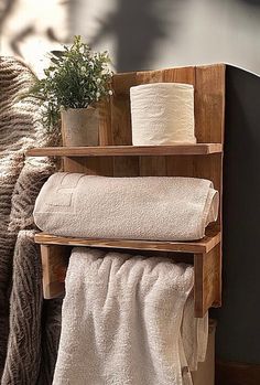 a wooden shelf holding two rolls of toilet paper next to a potted plant and towel rack